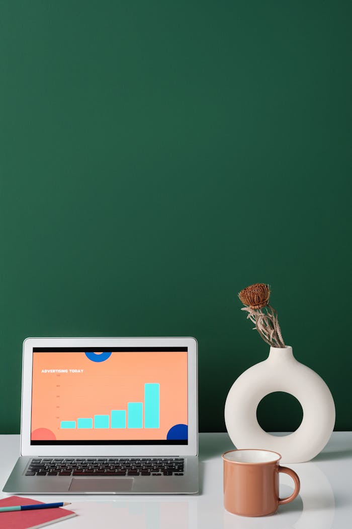 A minimalist workspace featuring a laptop with graphs, a stylish vase, and a coffee cup on a sleek surface.