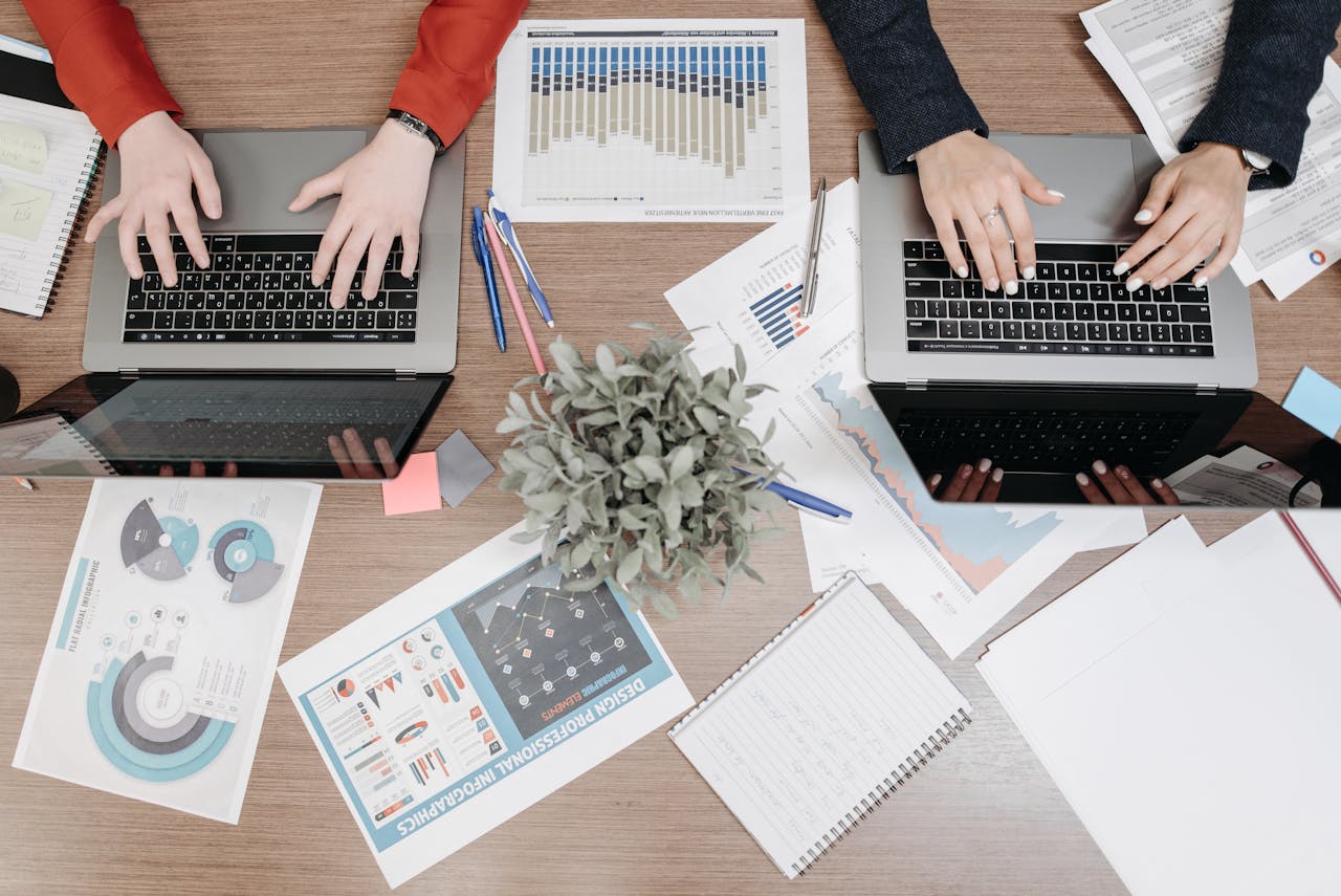 High-angle view of colleagues working on laptops with reports and charts in an office setting.